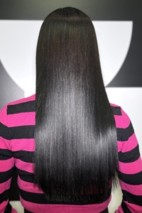Back view of a person with long, straight black hair wearing a pink and black striped sweater.