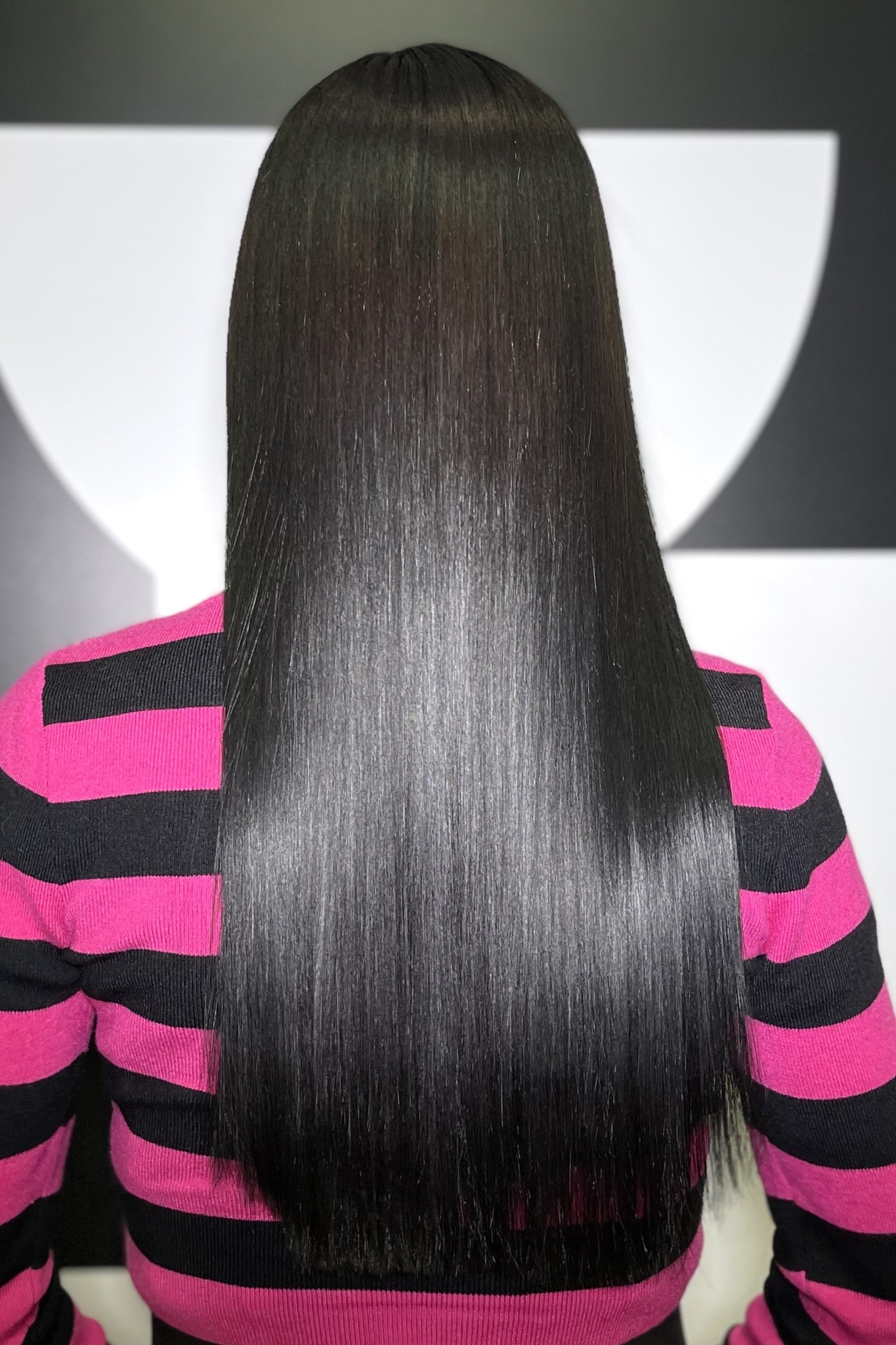 Back view of a person with long, straight black hair wearing a pink and black striped sweater.