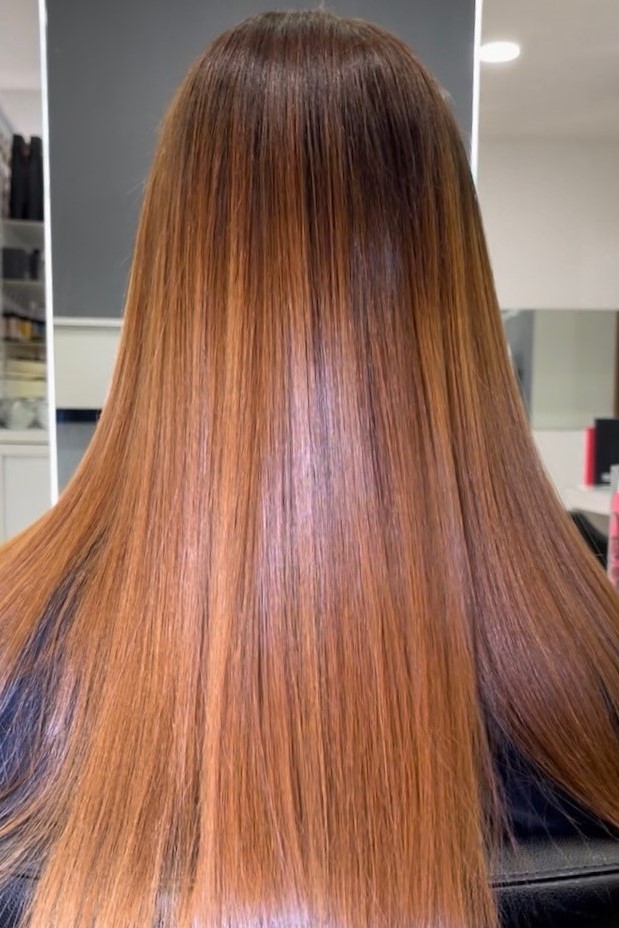 Hairlifting il liscio Assoluto Back view of a person with long straight copper-brown hair reaching mid-back in a salon setting.