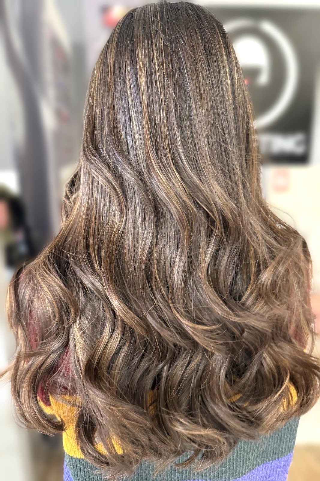 Back view of long wavy brown hair with caramel blonde highlights, resting on a multicolored knit sweater.