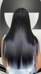 Back view of a person with long, straight, glossy black hair that fades to light blue at the ends, wearing a light denim jacket.