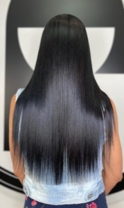 Person with long, straight black hair with blue ombré ends, seen from behind in a denim vest or jacket.